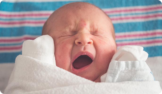 Newborn baby swaddled and yawning